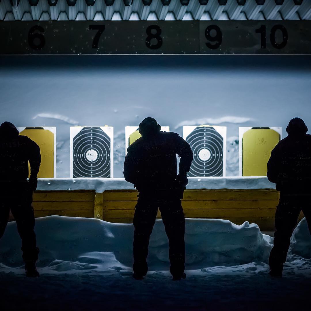 Värikuva, jossa talvella kolme henkilöä on valmistautumassa ampumaan maalitauluun ampumaradalla. Taulujen yläpuolella on numeroita.