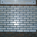 Tiiliseinään on kiinnitetty vaaleita laattoja, joissa on henkilön nimi ja kuolinaika. Päällä iso laatta, jossa teksti: Itsenäisyyden aikana palveluksessa väkivallan kautta surmansa saaneet poliisimiehet.