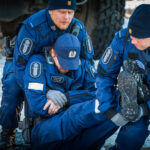 Värikuva harjoitustilanteesta, jossa kaksi virkapukuista poliisia auttaa kolmatta, loukkaantuneen oloista poliisia.