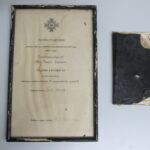 Vanha kehystetty kunniakirja ja sen vieressä tummakantinen kulunut mustakantinen vihko.