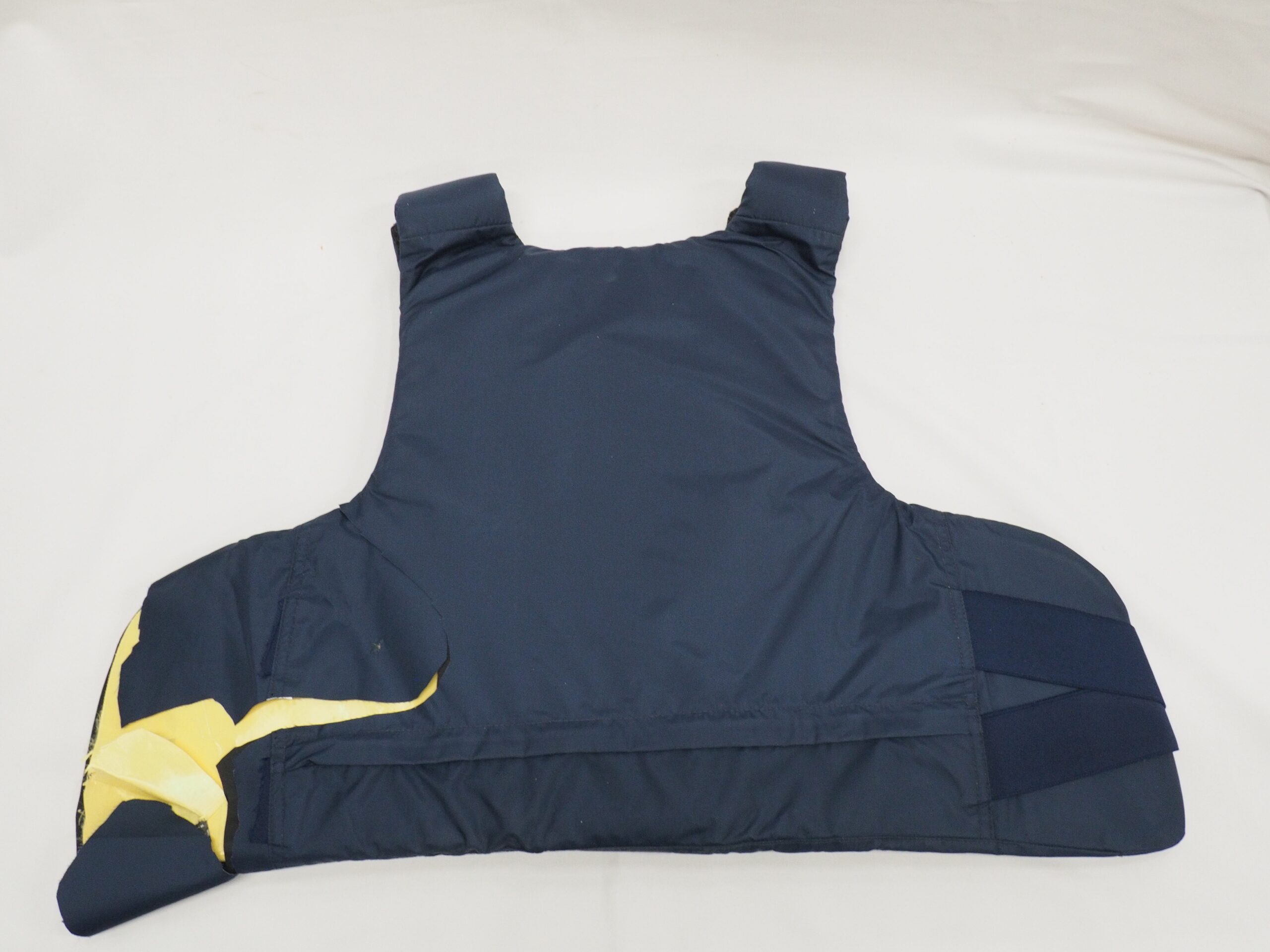 Tummansininen suojaliivi, joka on rikkoutunut vasemmassa alakulmasta.