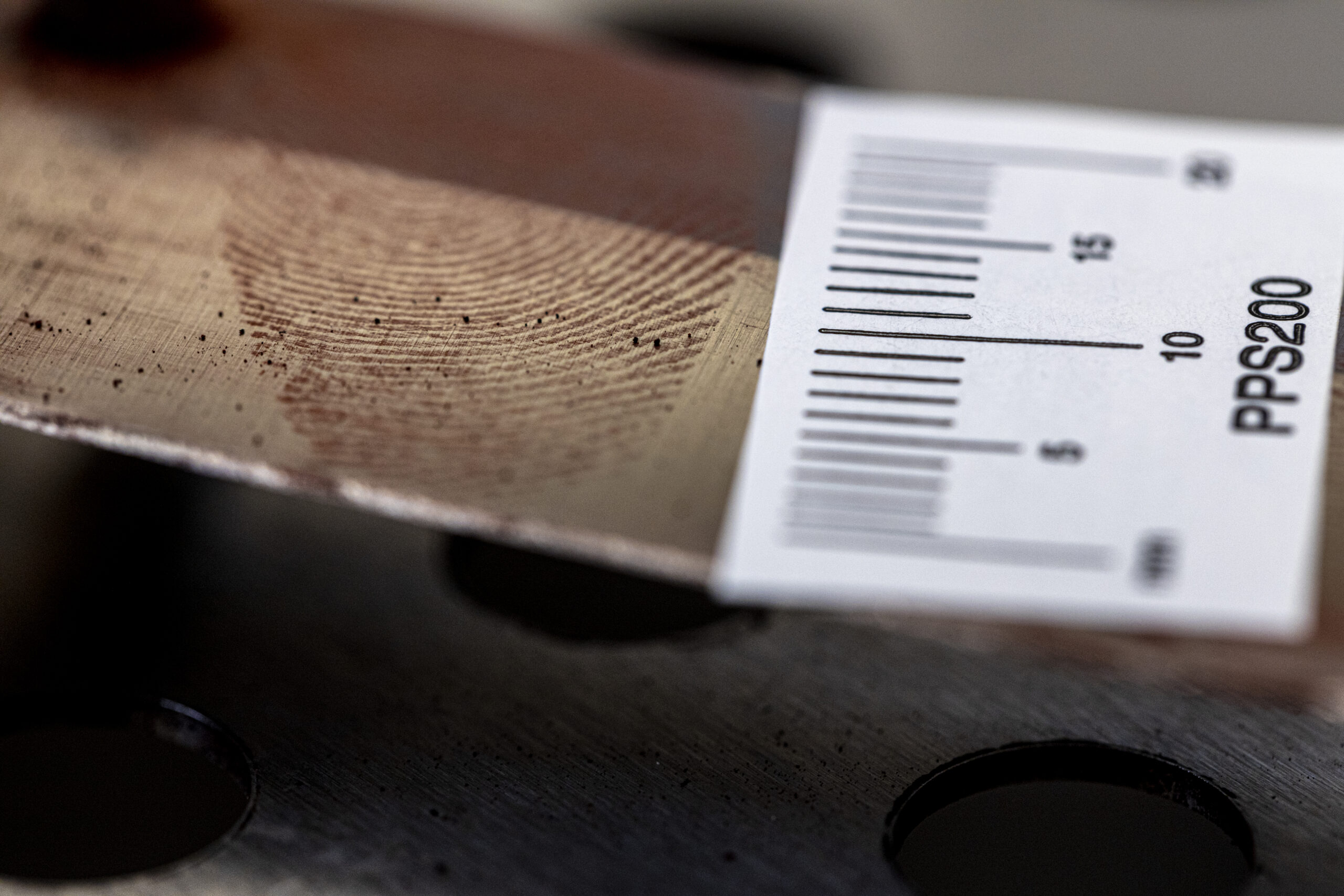 Värikuva, jossa poliisin käyttämä mitta on asetettu todistuskappaleen viereen. Esine metallinvärinen ja siinä on sormenjälki.