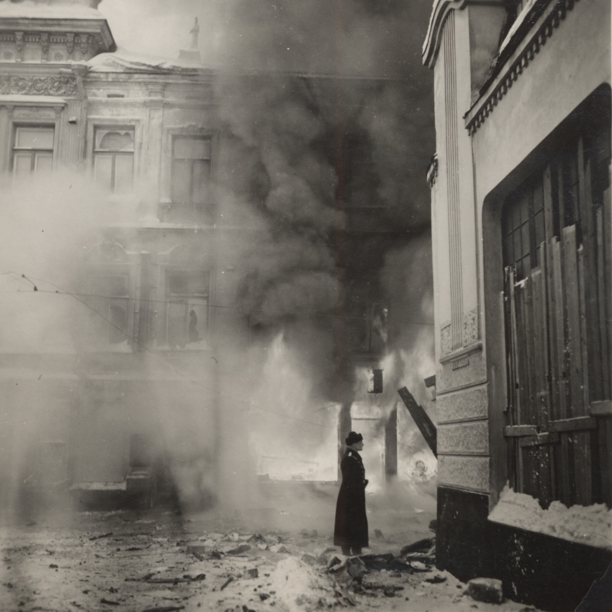 Mustavalkoisessa kuvassa katu on täynnä sankkaa savua. Keskellä seisoo tummiin pukeutunut poliisi, ja ympärillä näkyy kaupunkirakennuksia.