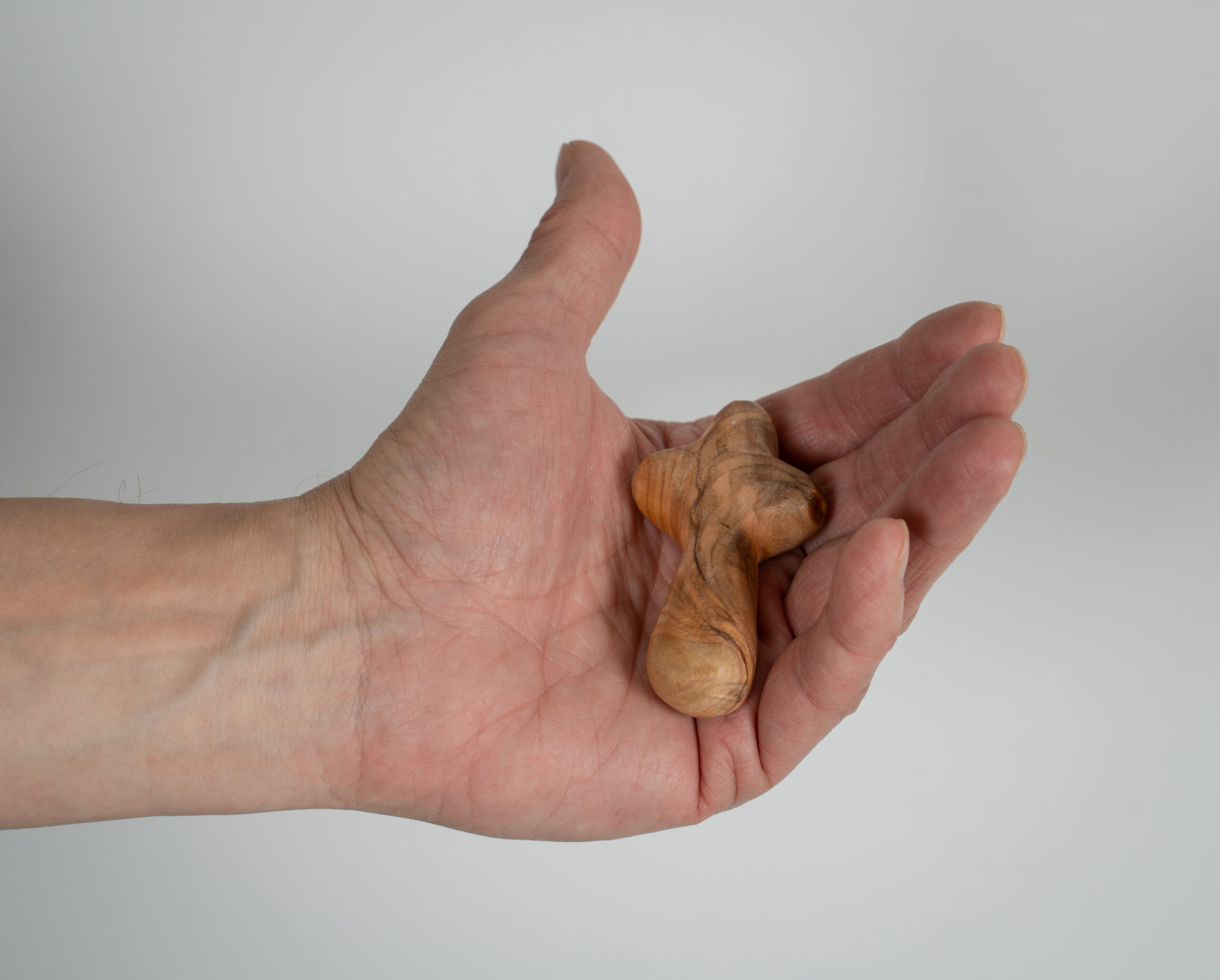 Lähikuva ihmisen kädestä, joka pitää kämmenellään pientä, puista ja pyöreäreunaista ristiä.